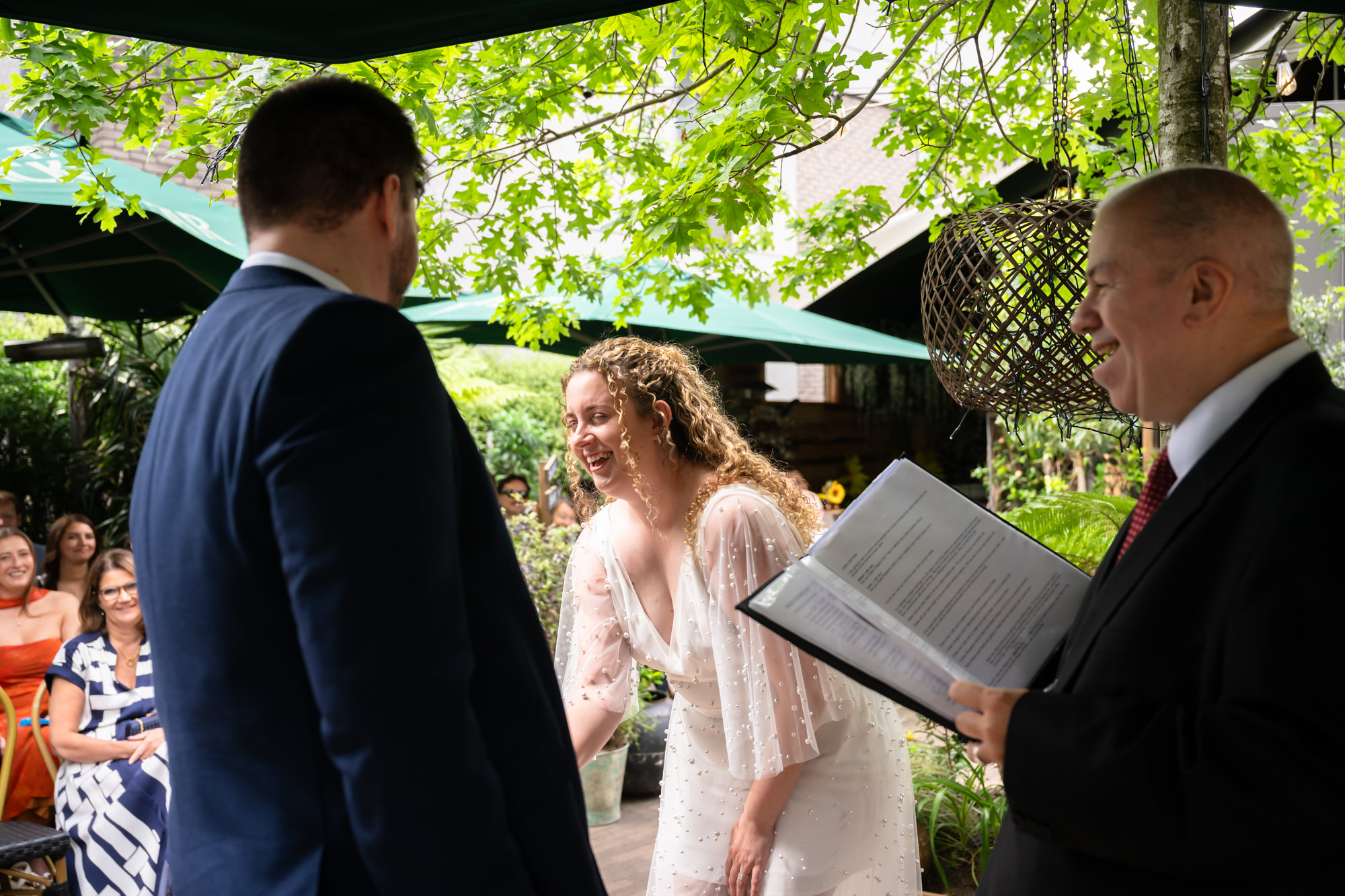 Bride laughing during the ceremony as the celebrant reads from a book behind her