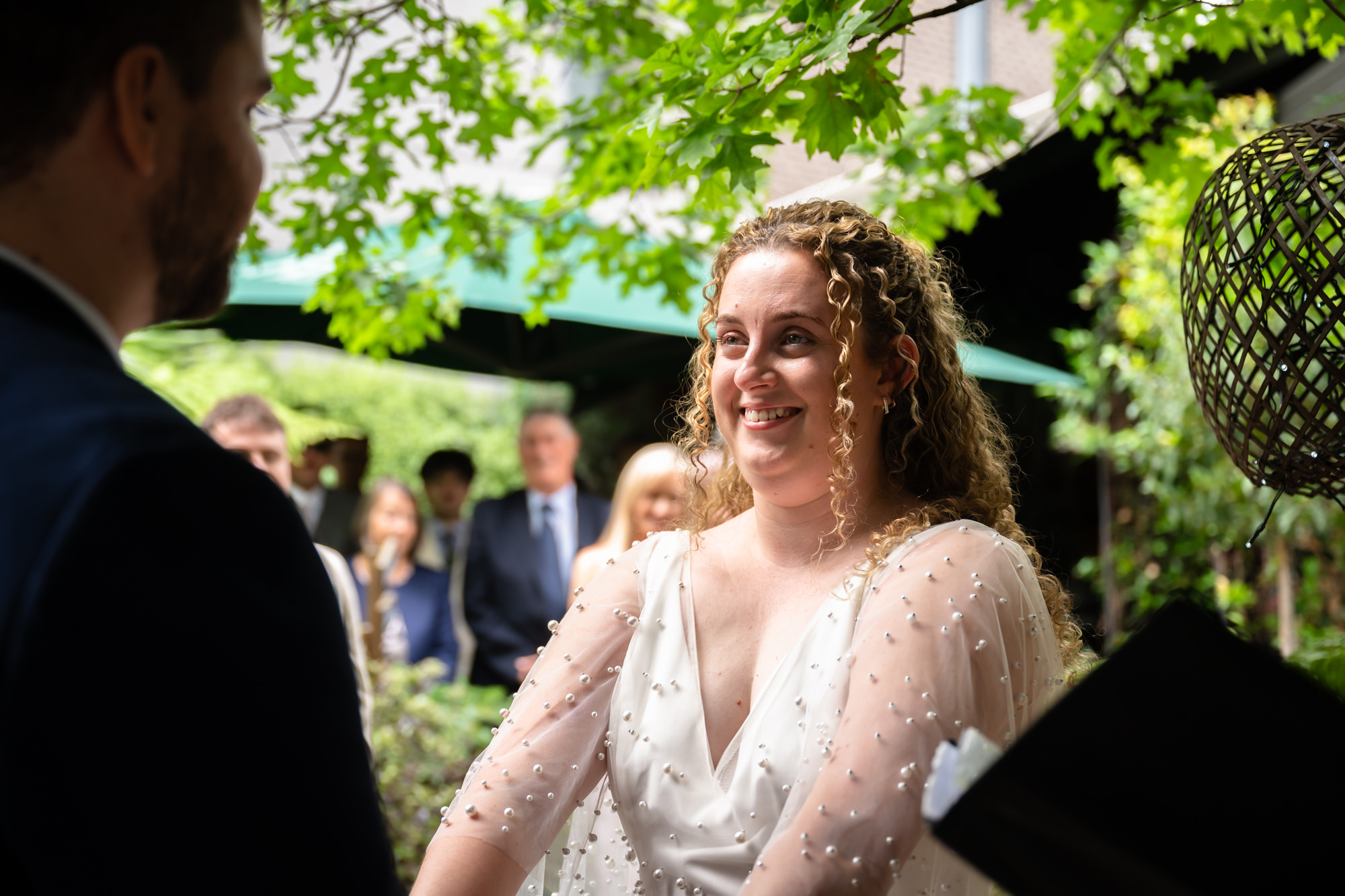 Bride smiling during the ceremony, wedding guests seated in the background