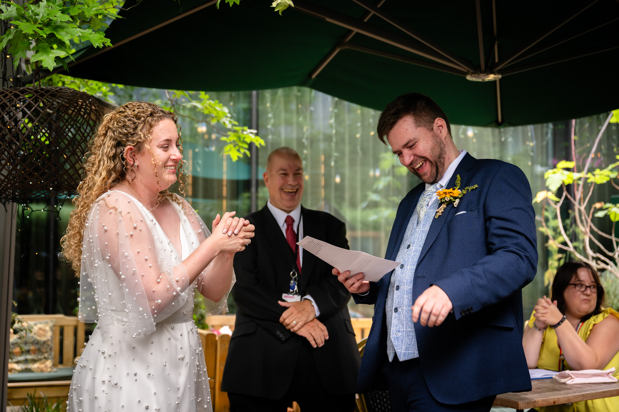 Bride and groom laughing and holding hands as the celebrant reads the vows