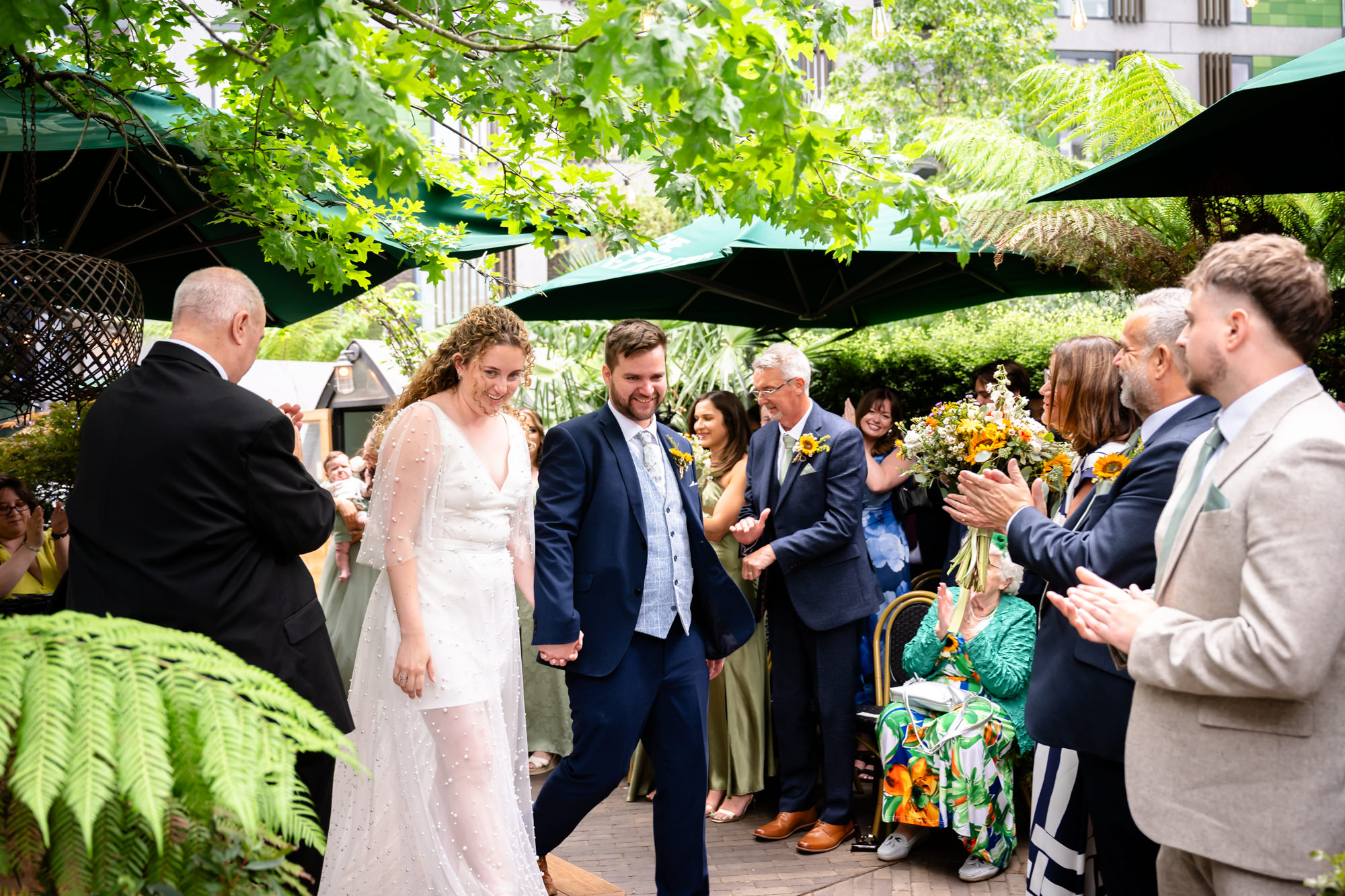 Newlyweds walking hand in hand as guests applaud after the ceremony