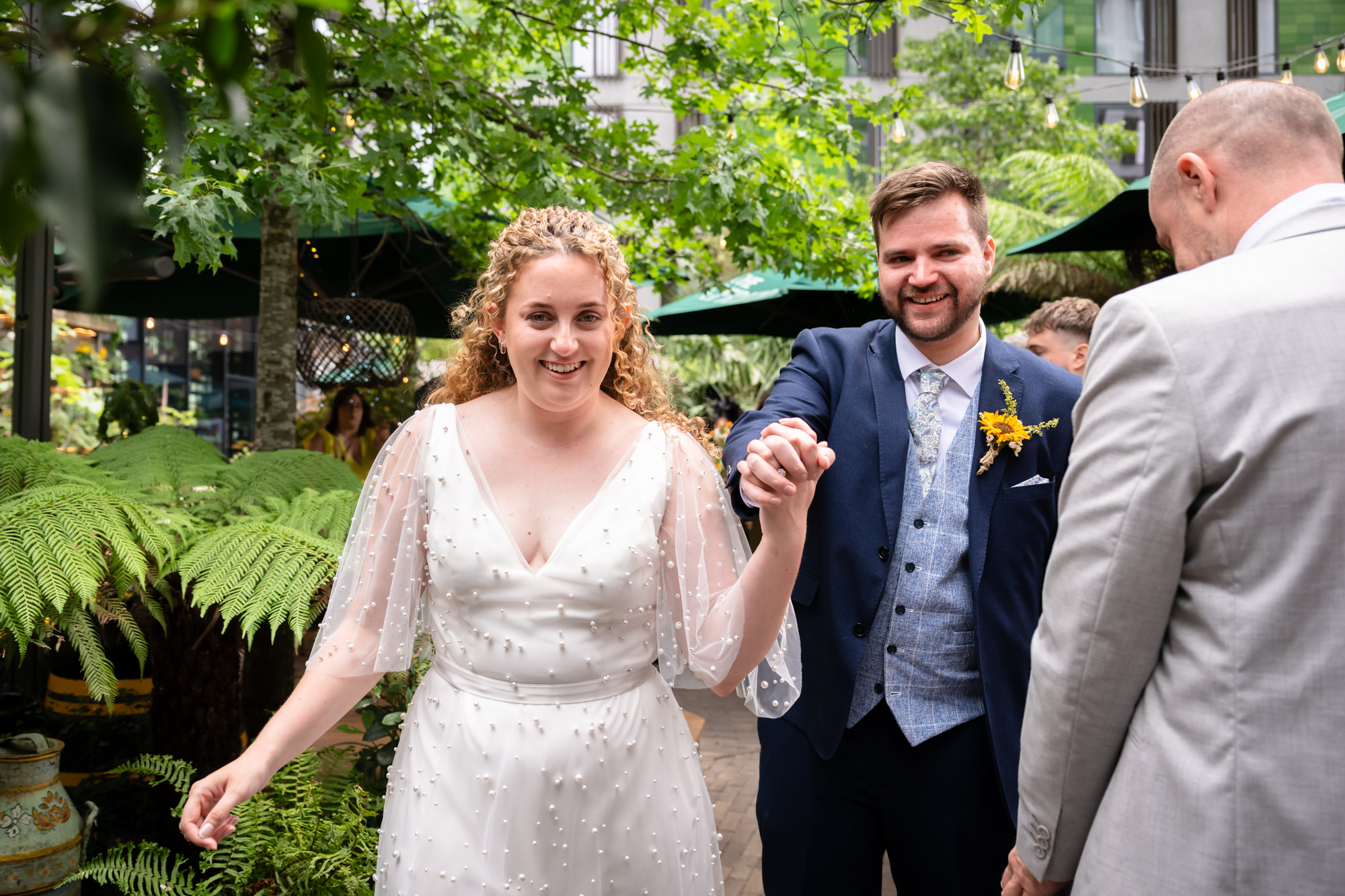 Newlyweds smiling and holding hands as they walk through the garden after the ceremony