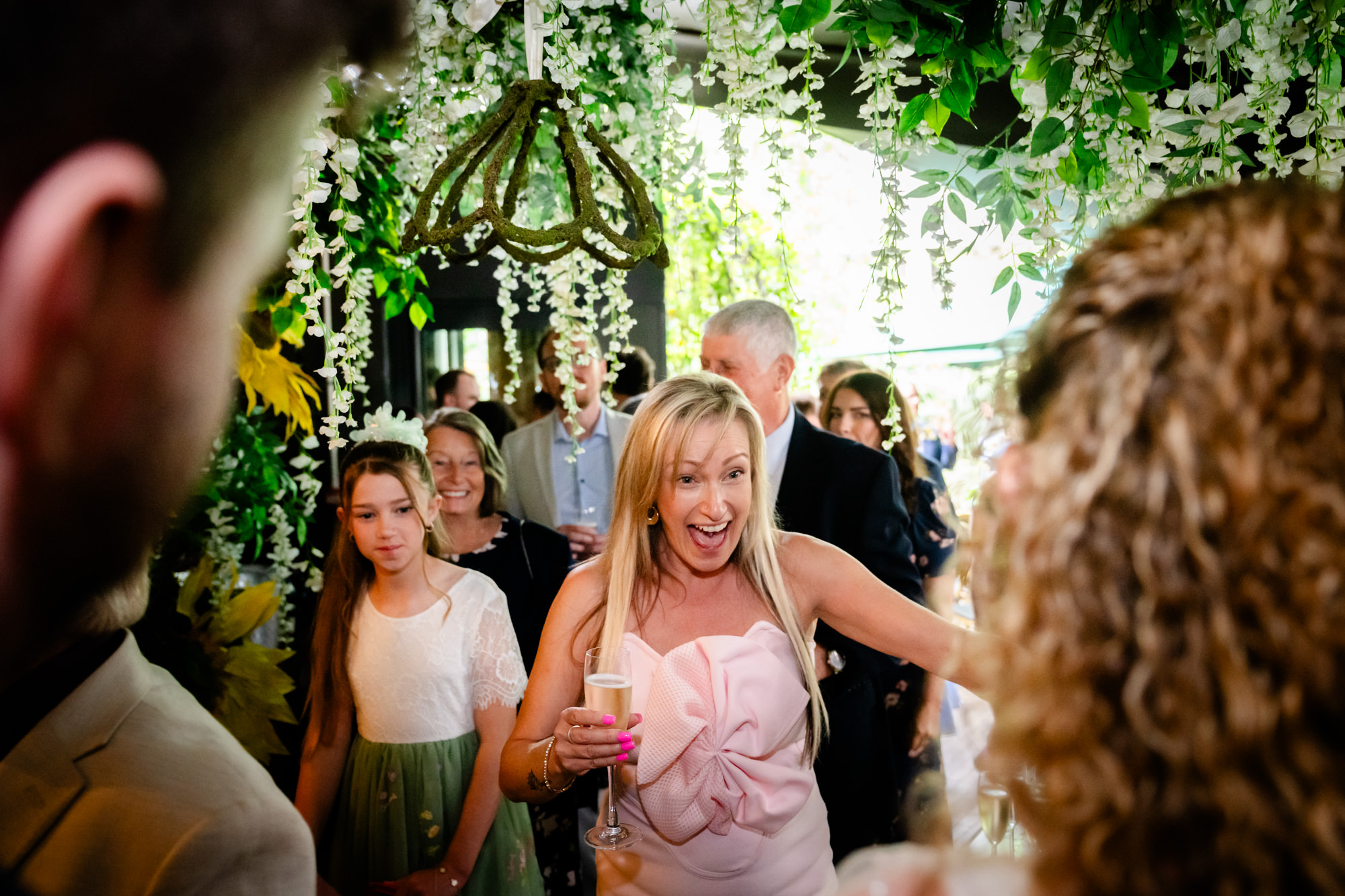 Wedding guest reaching out and laughing under a floral arch at the drinks reception