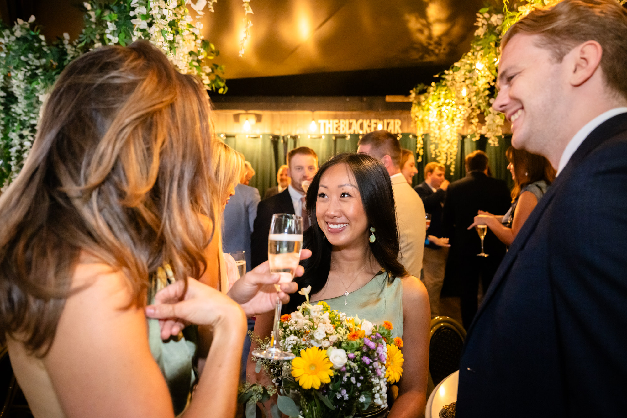 Bridesmaid toasting with champagne under wisteria decorations, Black Friar sign visible