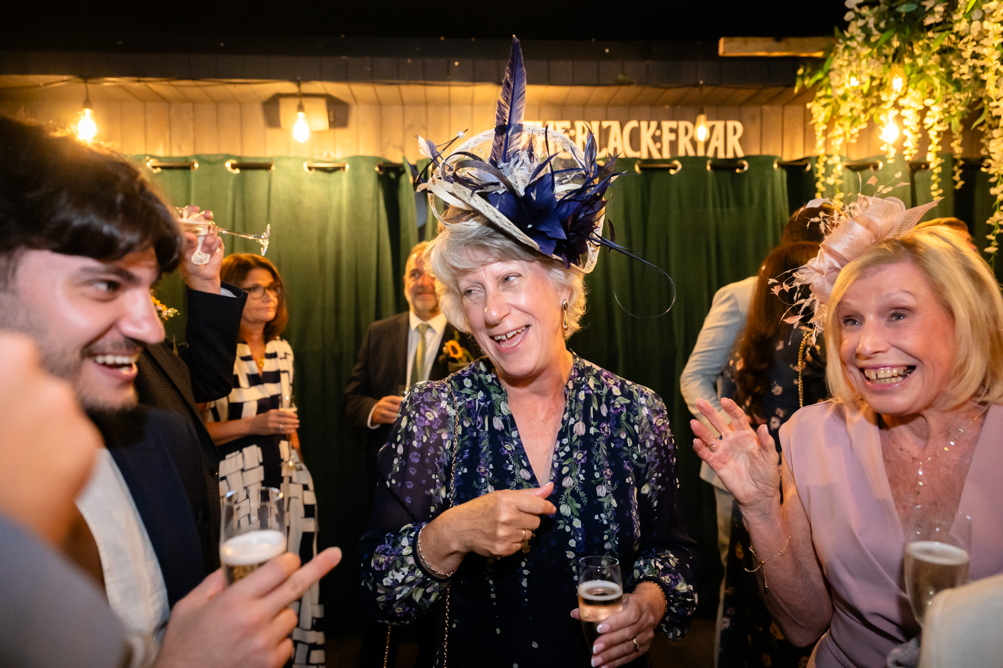 Wedding guest in a feathered fascinator laughing among others at the drinks reception