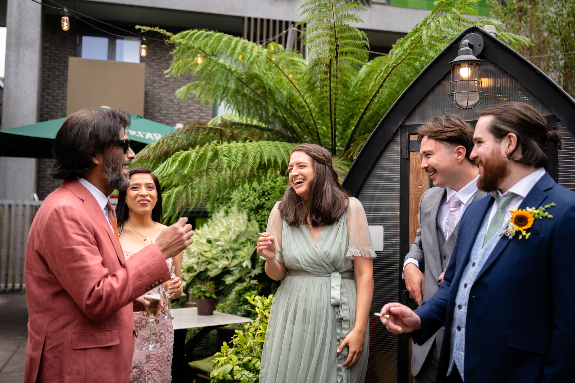 Group of wedding guests laughing together in the garden at the drinks reception