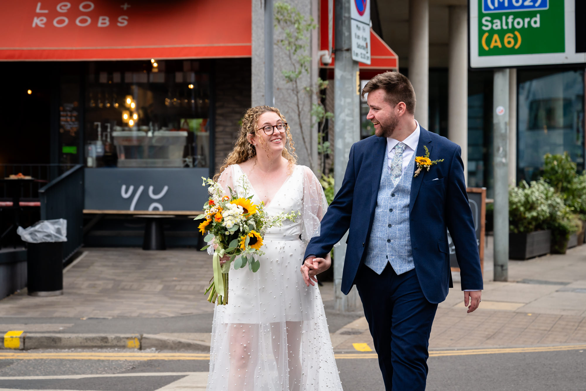 Bride and groom walking past a café near the Black Friar Salford, laughing together