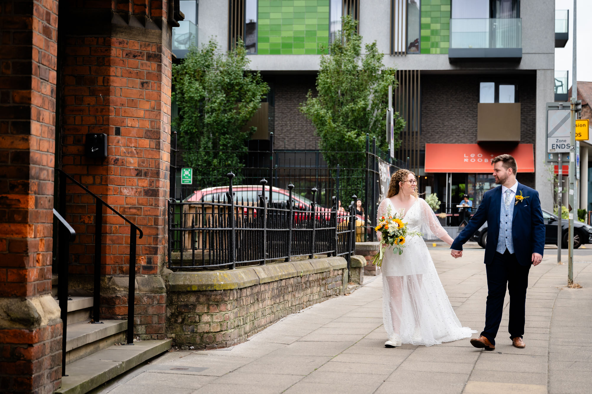 Bride and groom walking hand in hand along a street near the Black Friar Salford