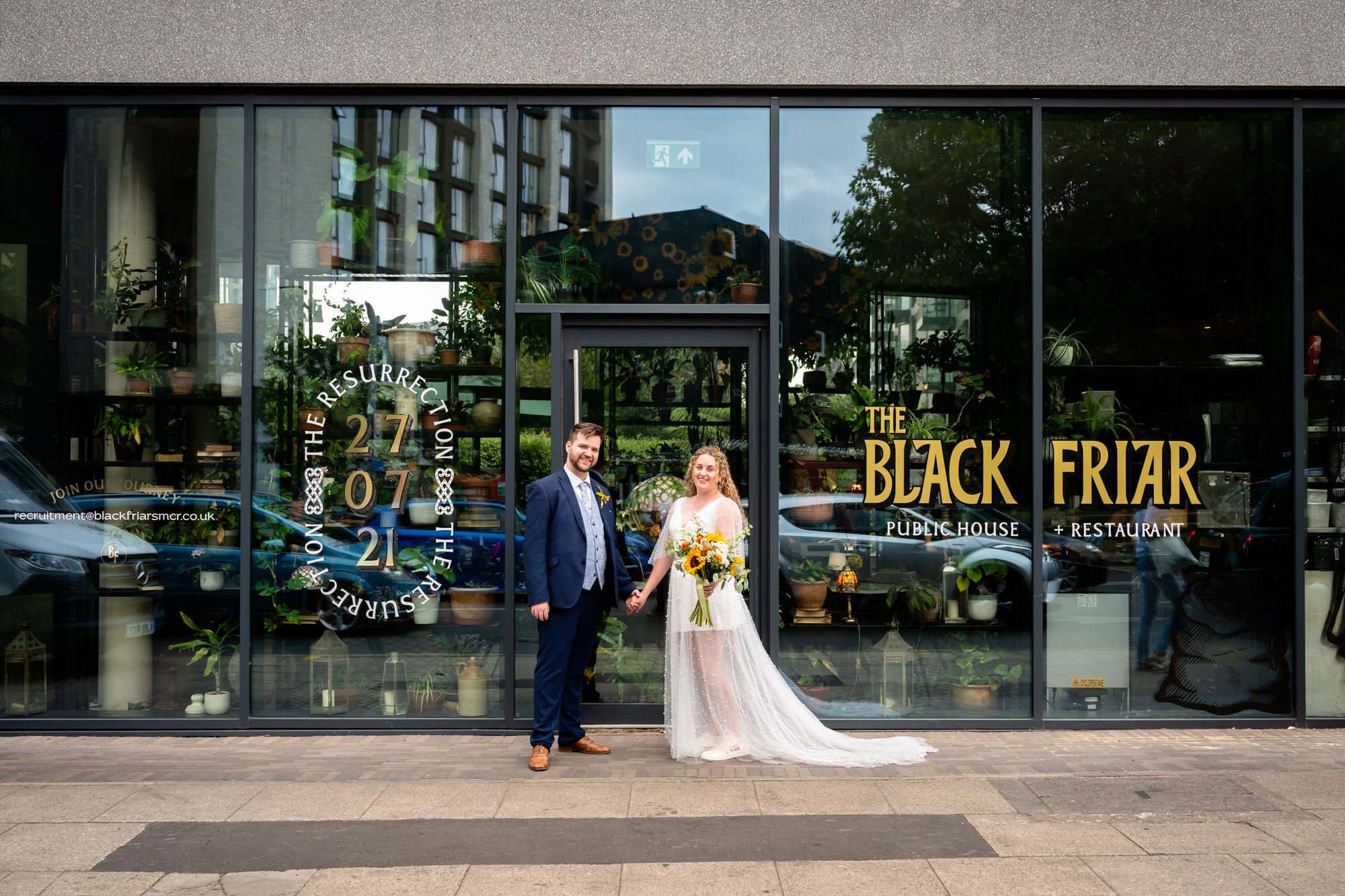 Bride and groom standing outside the Black Friar's glass frontage, holding hands