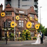 Bride and groom standing outside the Black Friar pub, exterior decorated with giant sunflowers