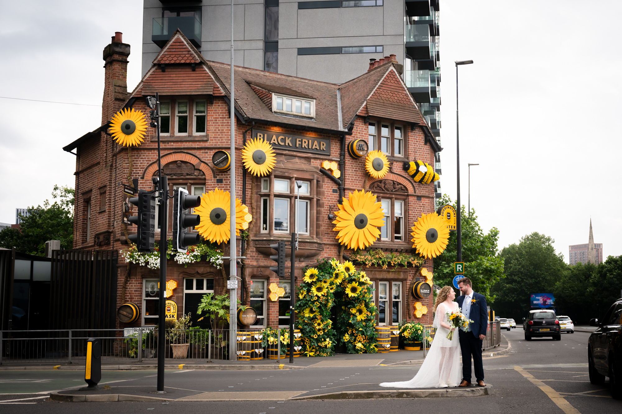 Bride and groom standing outside the Black Friar pub, exterior decorated with giant sunflowers