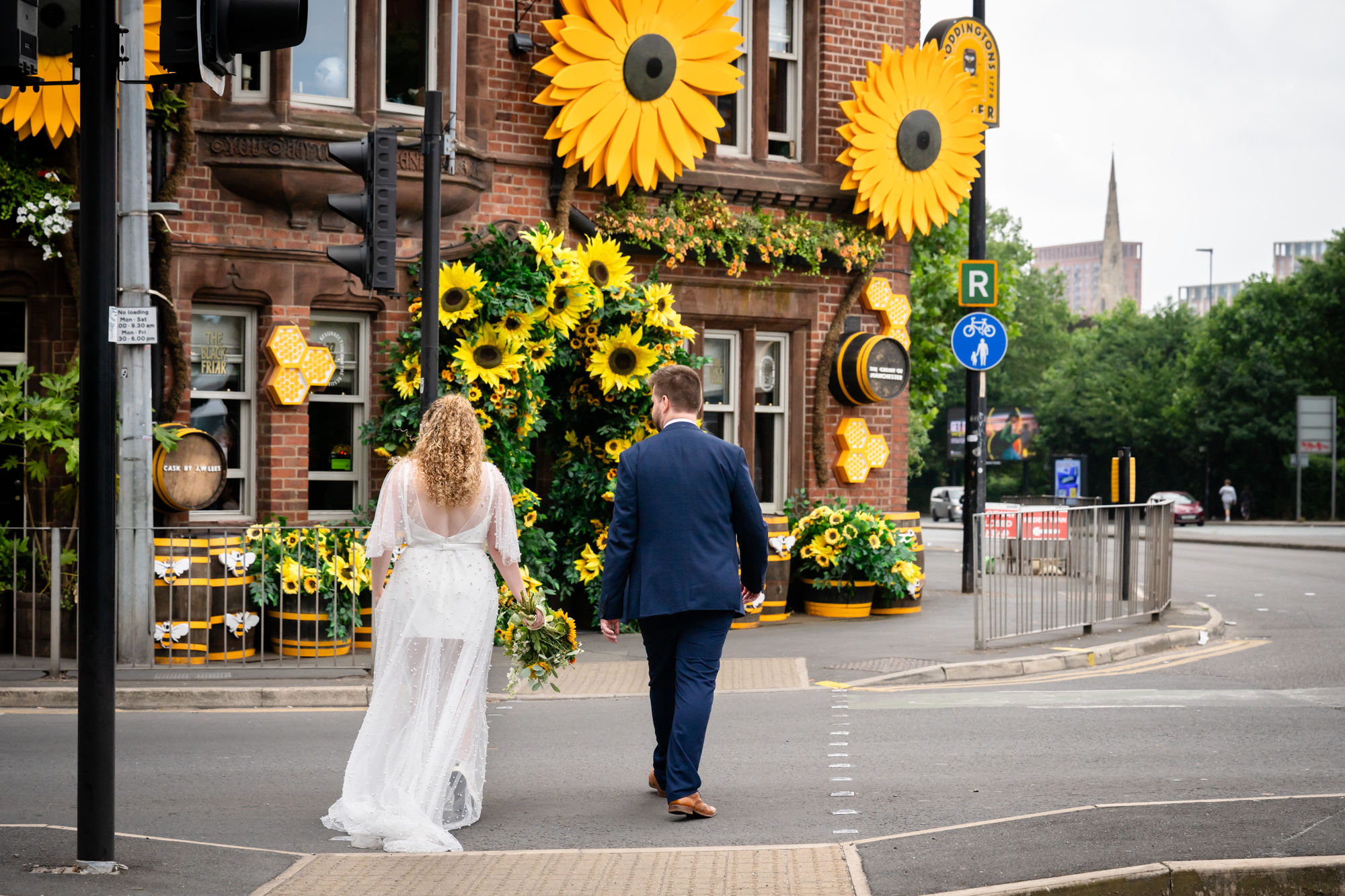 Bride and groom walking towards the sunflower-decorated entrance of the Black Friar Salford