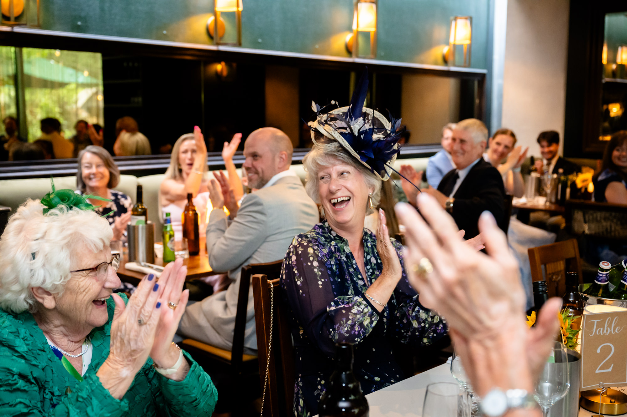 Wedding guests in fascinators clapping and laughing during the speeches