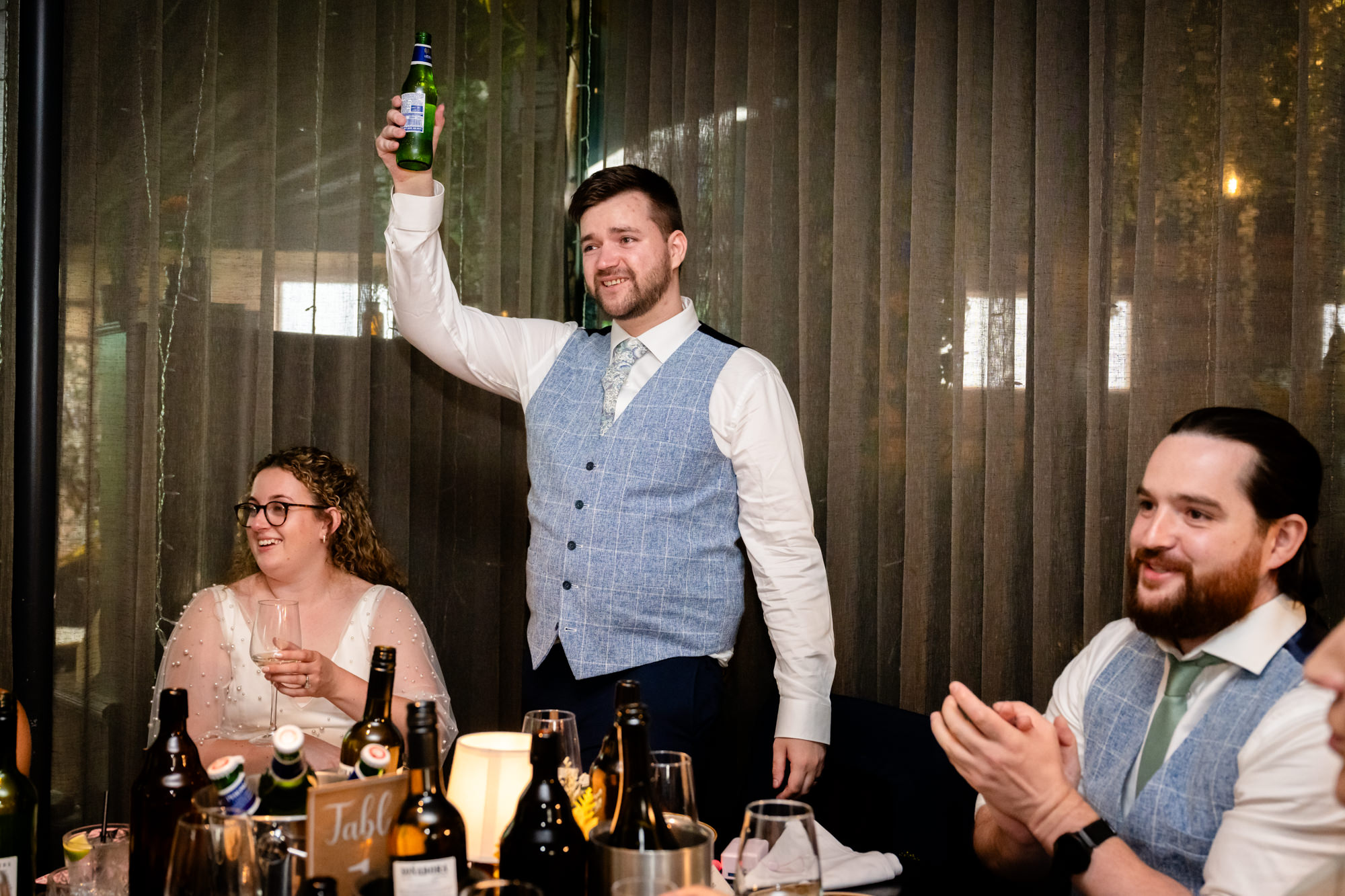 Wedding guest raising a bottle in a toast during his speech, guests applauding