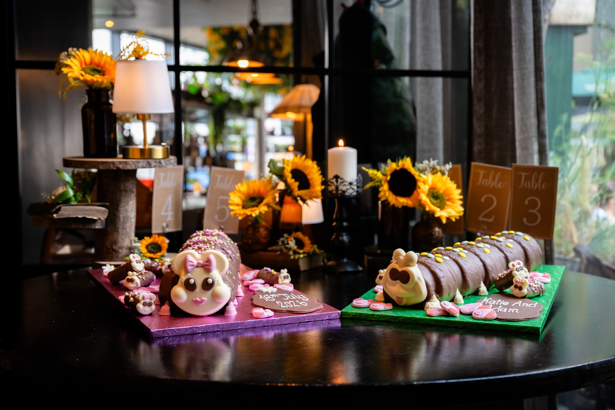 Two chocolate caterpillar wedding cakes on a table with table number cards