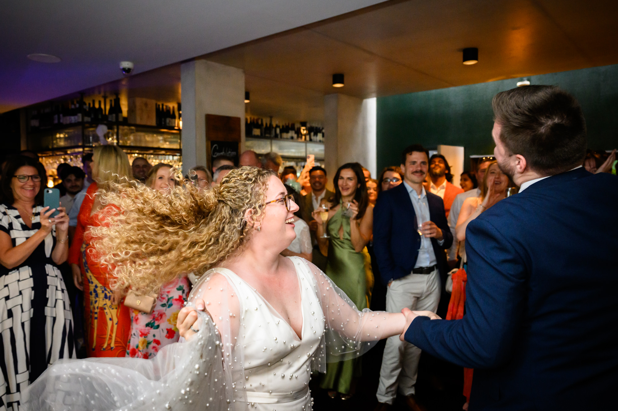 Bride's hair flying as she dances with the groom, guests clapping in the background