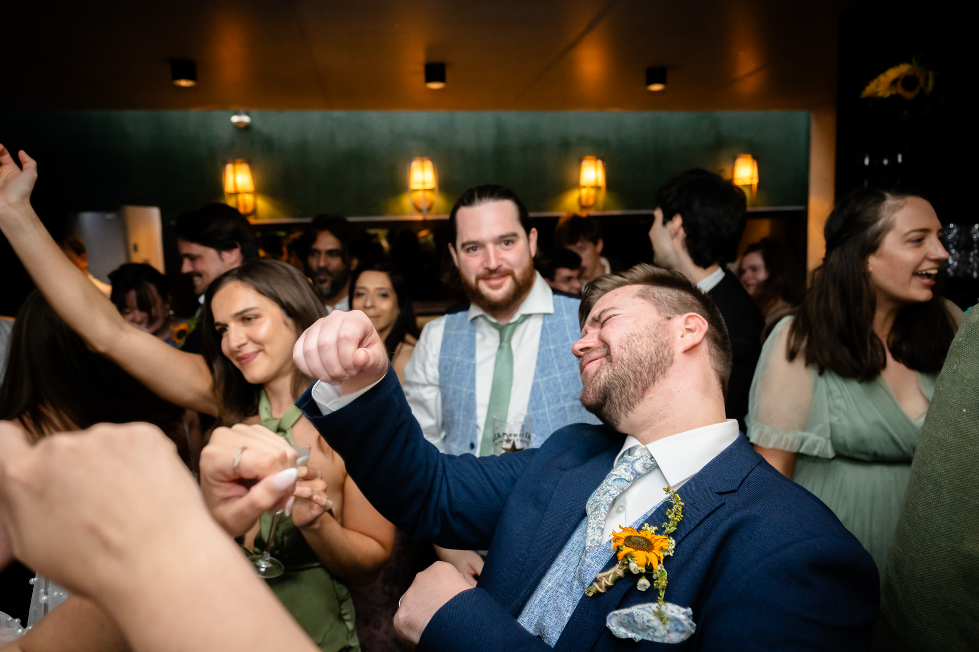 Wedding guest fist pumping while dancing, guests laughing around him