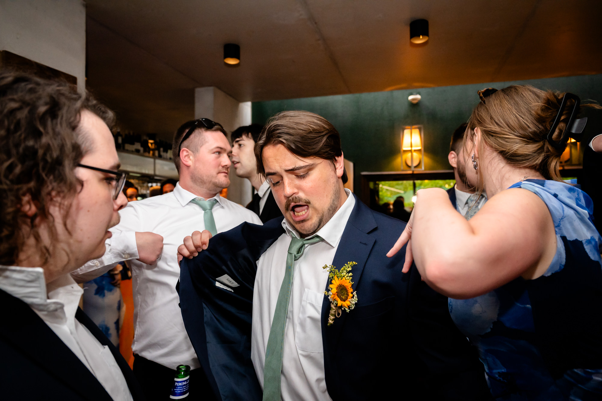 Wedding guest dancing while playing with his jacket, friends laughing beside him