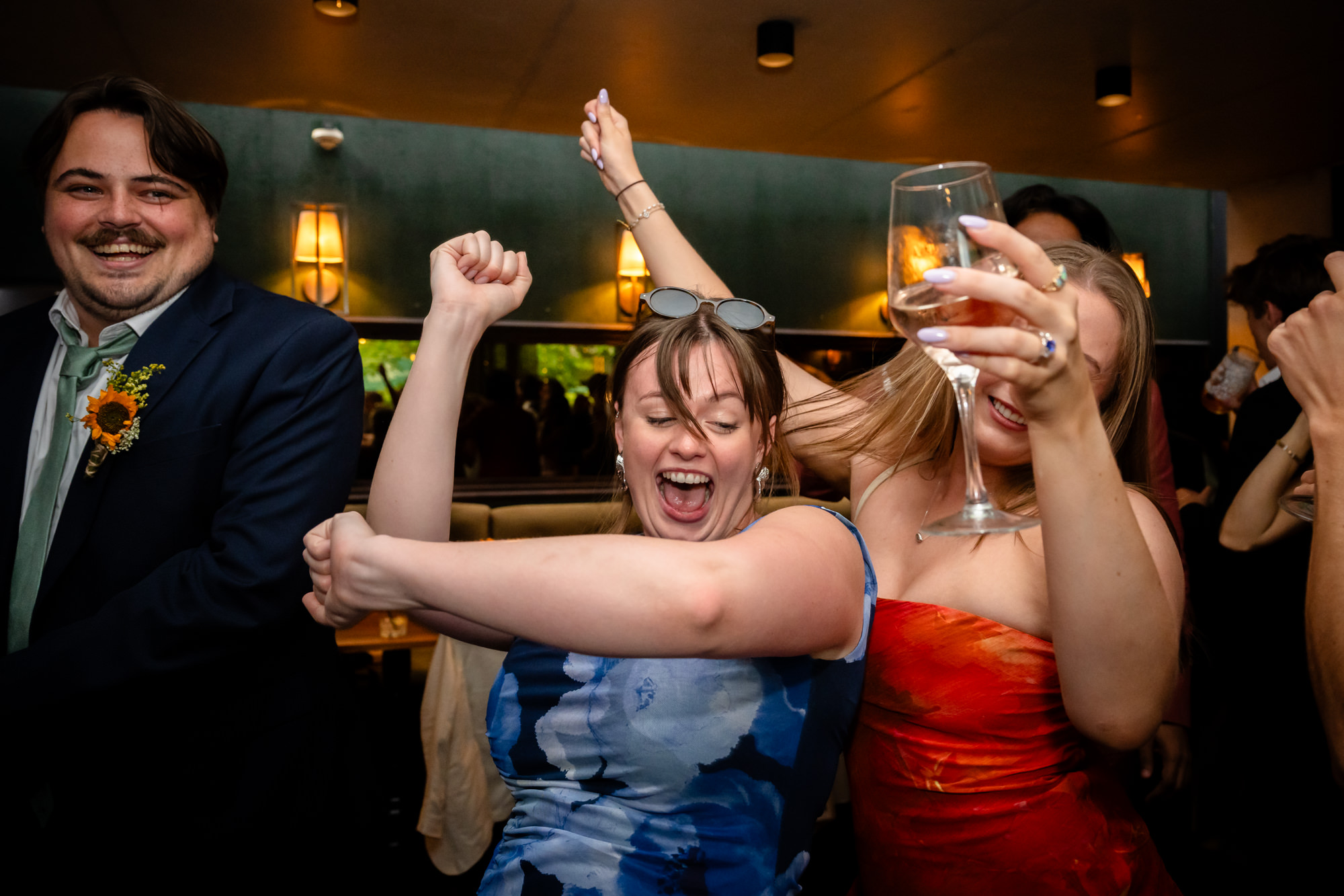 Wedding guests dancing with arms raised, one holding a glass of wine