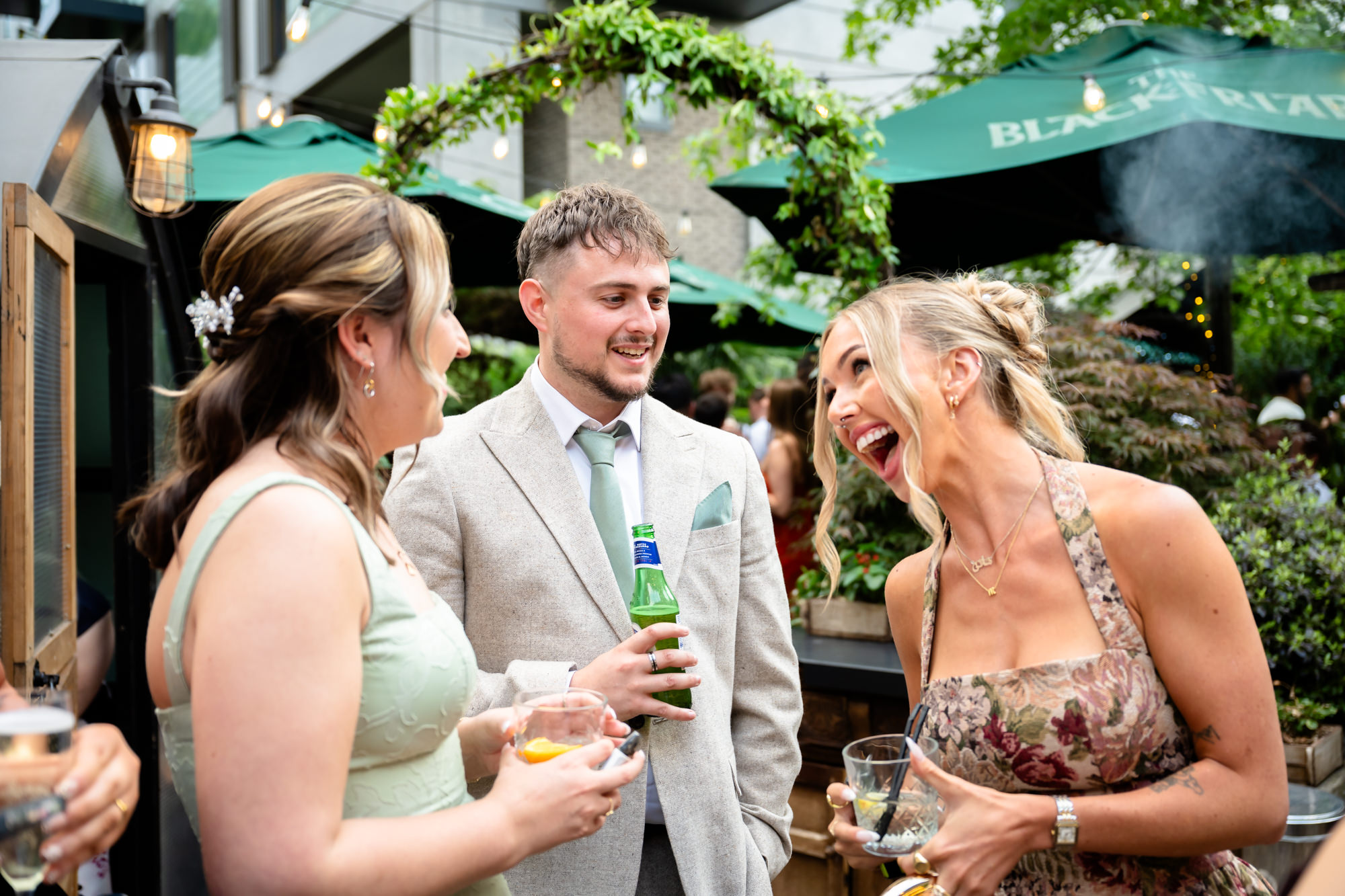 Wedding guests laughing together outside the Black Friar in the evening