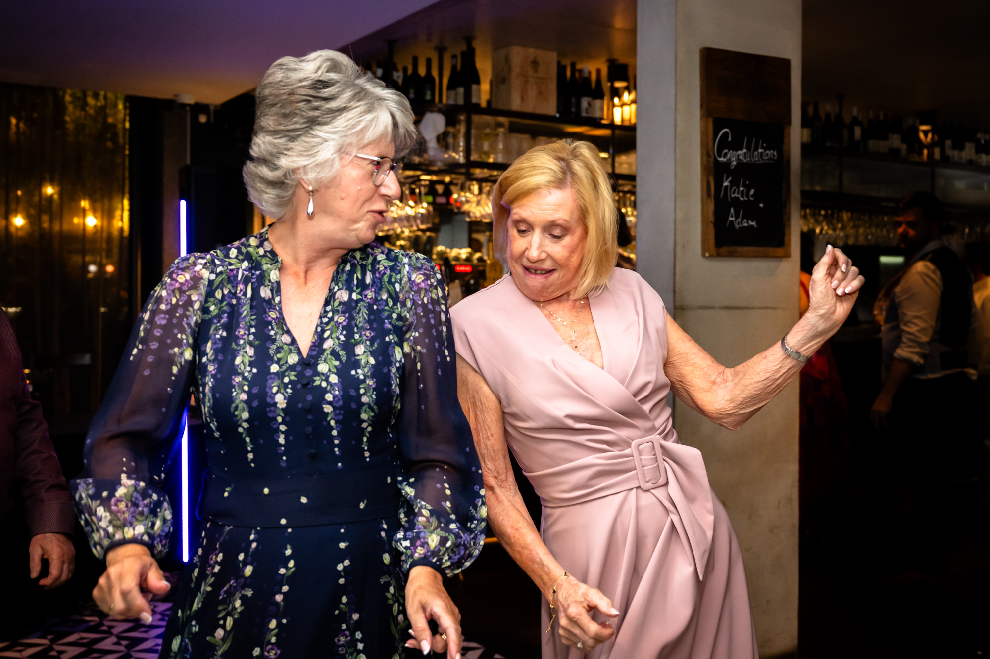 Two older wedding guests dancing together by the bar