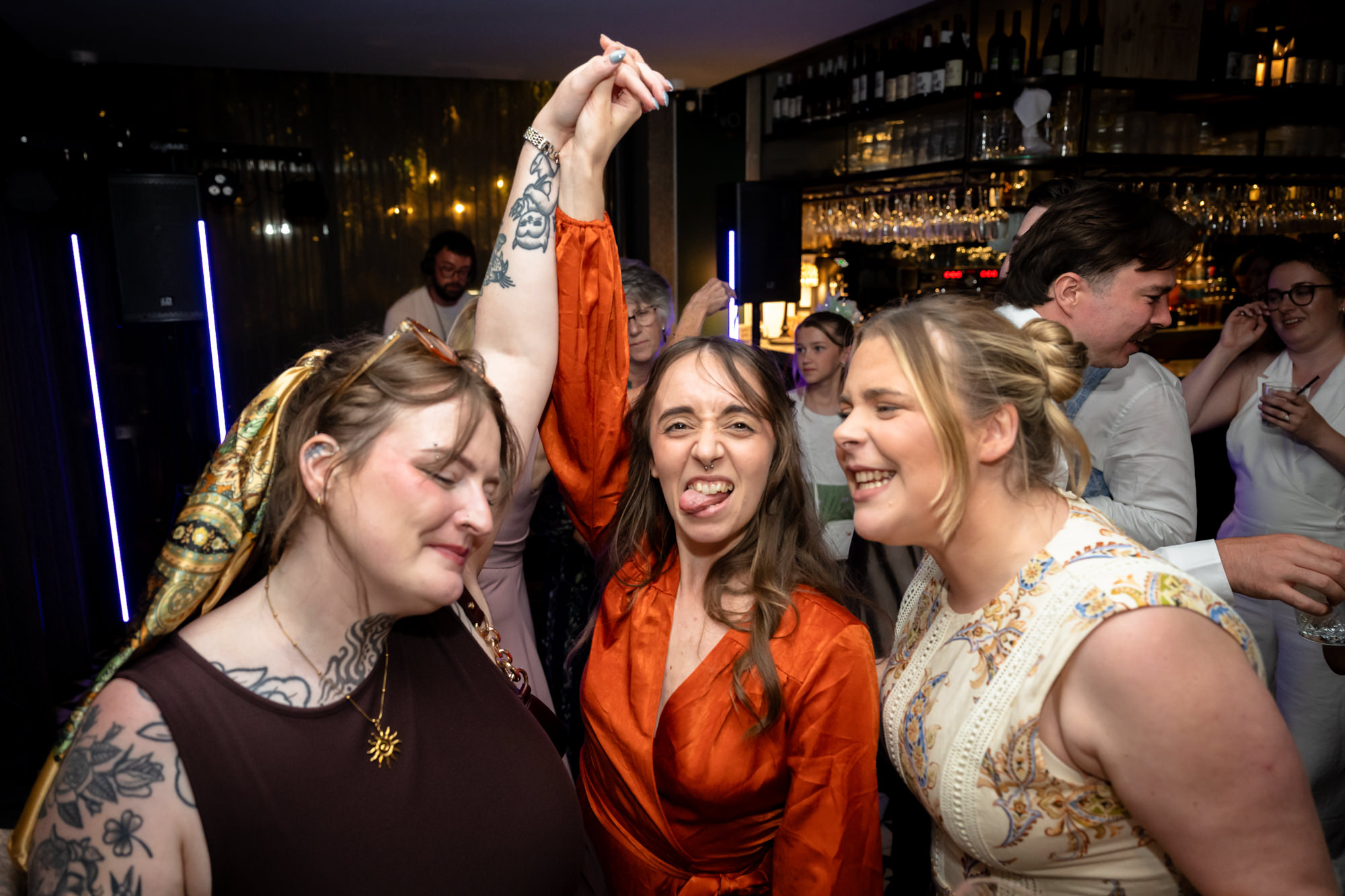 Three wedding guests laughing together, one sticking her tongue out