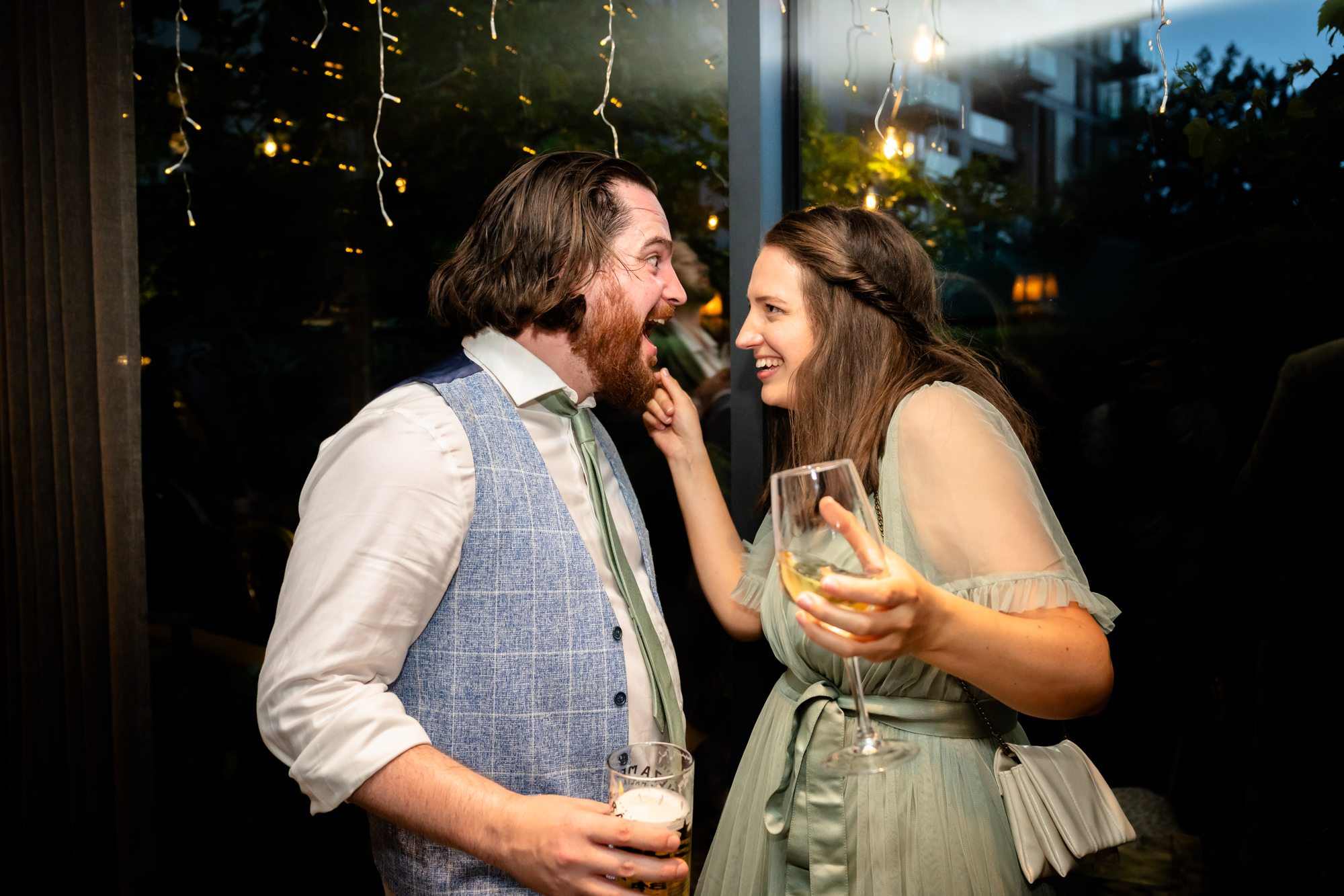 Wedding guests laughing together, one playfully touching the other's beard